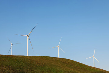 Wind power turbines on the green hill lover the blue sky.