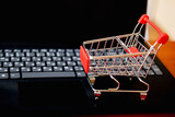 Fototapeta Tęcza - Online shopping. Supermarket cart on open laptop. E-commerce, buying goods or services over the Internet, buying goods in online stores using the concept of digital technology.