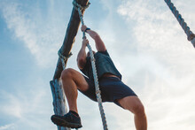 Below-view Of A Strong Male Pulling Himself Up A Rope Against Blue Sky