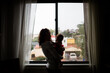 © Cavan Images - Late Thirties Mother Holding Baby in Front of Window for Silouette