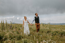 Bride And Groom Walk Through Field Of Wildflowers In Wyoming