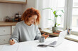 © shurkin_son - Cheerful woman ceo manager working online at kitchen table with cup of coffee, phone and copybook, having video conference with partners, discussing agreement, gesticulating looking at laptop screen