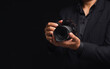 © meeboonstudio - Photographer in a suit holding the digital camera while standing on a black background