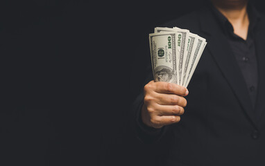 Businessman holding US dollar bills while standing on a black background