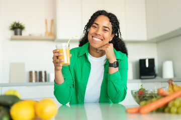 Wall Mural - Cheerful African American Woman Drinking Fresh Orange Juice In Kitchen