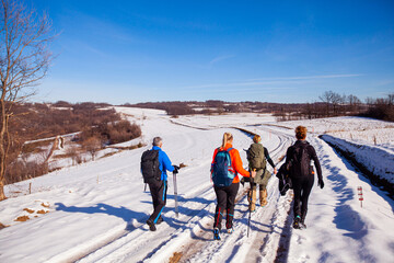 Canvas Print - Rear view a group of people hiking on winters trail. Rural road covered by snow. Winter adventure journey. Winter nature landscape.	