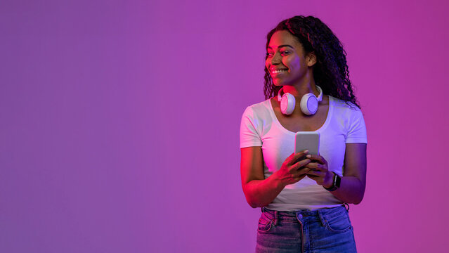 Wall Mural - Smiling Black Female Holding Smartphone And Looking Aside At Copy Space