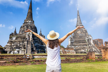 A happy tourist woman on a sightseeing trip stands in front of the buddhistic temple ruins at the historic city of Ayutthaya, Thailand