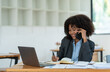 © crizzystudio - Young african american businesswoman sitting at the table in the office while making with a business colleague in receiving good news on modern business contracts.