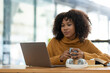 © crizzystudio - Young African businesswoman wearing headphones while looking at online shopping data Taking note of customer orders on a laptop while holding a mug of warm coffee to relax.