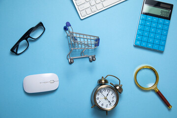 Wall Mural - Alarm clock, shopping cart on the blue background.