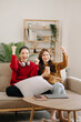© Nuttapong punna - Two asian beauty smiling young women sitting on sofa Attractive casual girl feel happy and relax,having fun watch comedy video on TV in house. Activity lifestyles concept.