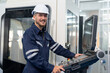 © Supachai - Male engineer operating cnc machine in control panel at factory. Smiling man technician in uniform and helmet safety working at workshop heavy metal industrial