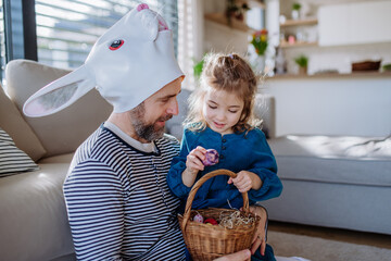 Wall Mural - Little girl with holding basket and showing her father with rabbit mask easter eggs which she found.