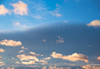 Wall Mural - blue and gray sky background with floating lighted cumulus clouds