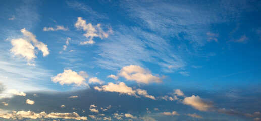 Wall Mural - blue and gray sky background with floating lighted cumulus clouds