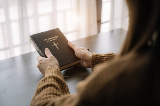 close up of an open bible with a cross for morning devotion on a wooden table with window lights.
