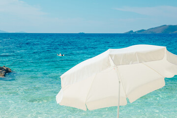 white sun umbrella clear blue water on background