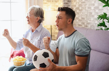 Caucasian couple of young boy soccer fan and elderly grandmother with disappointed expression while watching soccer match on tv sitting on comfortable sofa in living room