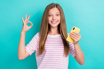 Poster - Portrait of charming schoolgirl hold cellphone hand fingers show okey symbol isolated on emerald color background