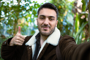 Young happy man making okey sign while taking selfie in forest. Nature love concept.