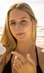 Caucasian blonde hair girl on the beach applying chemical free organic and vegan mineral sunscreen. Mention the beach, summer season with yellow and orange colors. Ocean waves with sun.