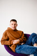 © Iryna Savchuk - Portrait of a young 30-year-old man. Brown sweatshirt and blue jeans. Purple stylish chair
