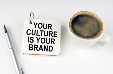 On a white surface, a cup of coffee, a pen and a notepad with the inscription - Your Culture is Your Brand