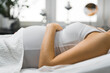 © PoppyPix - Woman touching her pregnant belly while laying on a bed. High quality photo