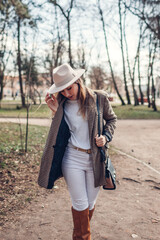 Wall Mural - Beautiful woman wearing stylish blazer hat and boots in park. Spring female fashionable outfit in white and brown color.