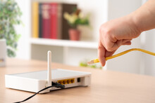 Close Up Of Man Hand Plugging Ethernet Cable To Router On A Desk At Home