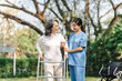 © NanSan - Young asian care helper with asia elderly woman on wheelchair relax together park outdoors to help and encourage and rest your mind with green nature. Help support yourself to learn to walk. walker