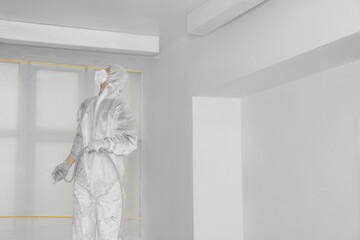 Canvas Print - Decorator in protective overalls painting ceiling with spray gun indoors