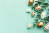Fototapeta Tulipany - Easter eggs painted in gold and eucalyptus branches on a soft green background.