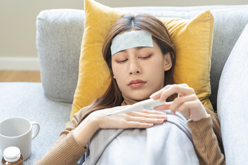 sick, influenza asian young woman put fever cooling patch on forehead, lying rest on sofa covered bo
