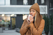 ill beautiful young woman sneezing and blowing nose in napkin. Sick businesswoman in business style sneeze at street. Unhealthy employee. Outdoor. Virus sympthoms. Cold disease.