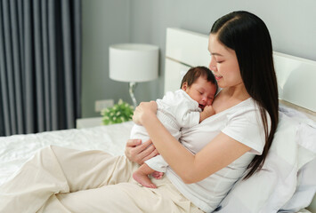 Wall Mural - mother holding and consoling her newborn baby to sleeping on bed