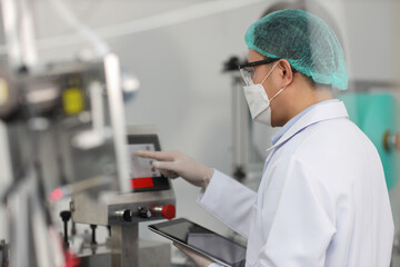 Poster - Worker man in personal protective equipment or PPE inspecting quality of mask and medical face mask production line in factory, manufacturing industry and factory concept.