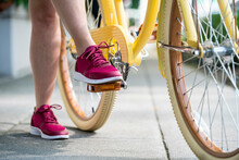 A Woman's Foot Steps On The Pedal Of Her Yellow Bike In Preparation To Ride