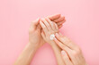 Young adult mother fingers applying white moisturizing cream on little girl hand on light pink table background. Pastel color. Care about baby clean and soft body skin. Closeup. Top down view.