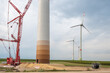 Construction site of a wind turbine, crane next to the tower of the wind turbine, completed wind turbines in background, cable reel, low angle view, cloudy day