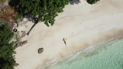 Wall Mural - Aerial view of relaxed woman at the tropical beach. Girl lying on the white sand with big hat. Tourism. Tourist. Traveler.