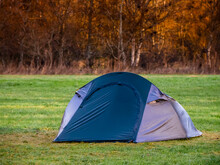 Blue Tent On A Green Grass In A Field Forest In The Background. Travel And Tourism Concept. Nobody. Active Outdoor Activity