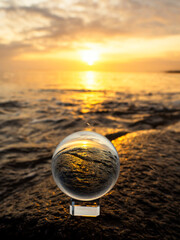 Wall Mural - glass ball on a rough stone by the ocean, sunset sky in the background. warm soft light. selective f