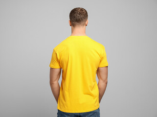Wall Mural - Man wearing yellow t-shirt on light grey background, back view. Mockup for design