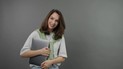 Wall Mural - A smiling, stylish office worker with a laptop on a gray background. Young woman posing inside