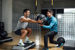 © BASILICOSTUDIO STOCK - Fitness personal trainer helping man with squatting pose with medicine ball