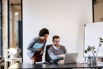 Wall Mural - A businessman is sitting at the office and pointing at the laptop while talking to a multicultural manager.