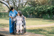 © NINENII - Young nurse covering disabled elderly woman in wheelchair with warm plaid, taking care of older female outdoors.