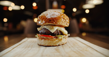 Close up zoom shot of large grilled appetizing burger with various ingredients on a wooden board - fast food, food preparation, unhealthy eating concept 